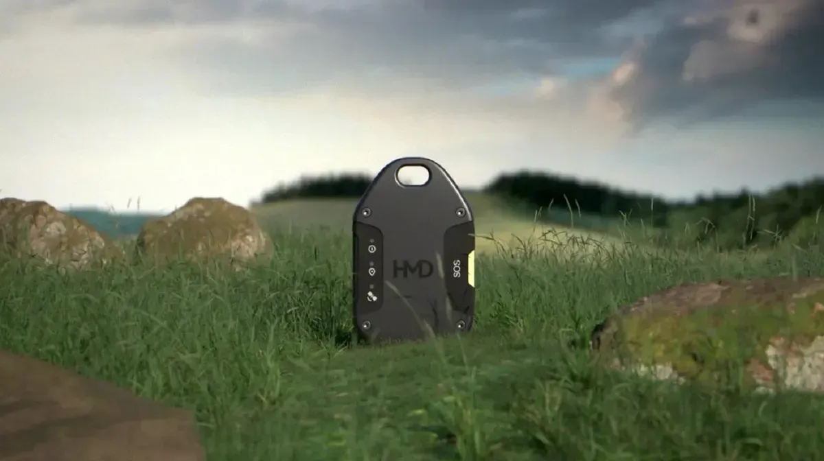 Black device in green grass field with rocks; cloudy sky in the background.