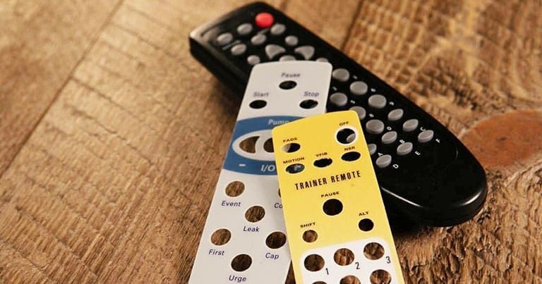 A black TV remote with two overlay templates, one white and one yellow, on a wood surface.