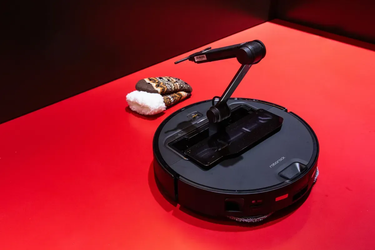 Robot arm on a robotic vacuum cleaner picks up food on a red surface.