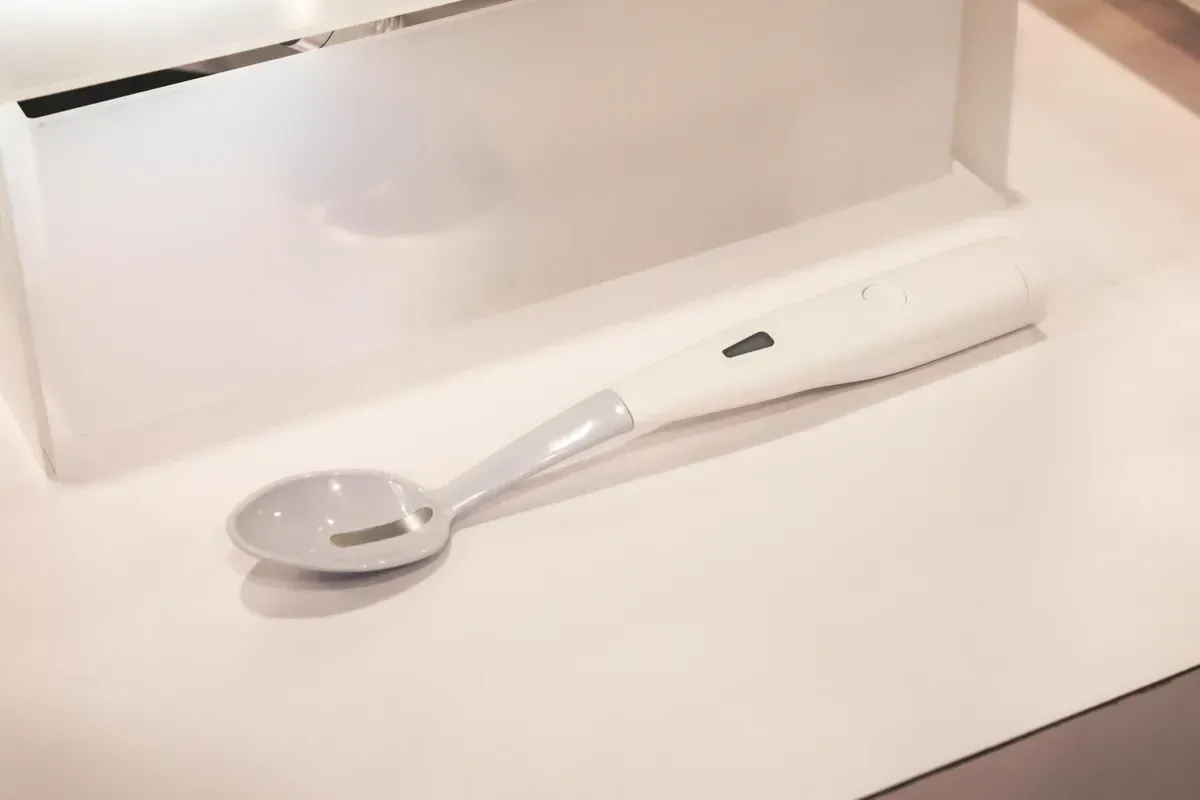 White electronic spoon on white surface, possibly for Parkinson's disease patients.