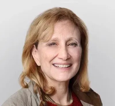 Smiling woman with shoulder-length blonde hair against a plain light background