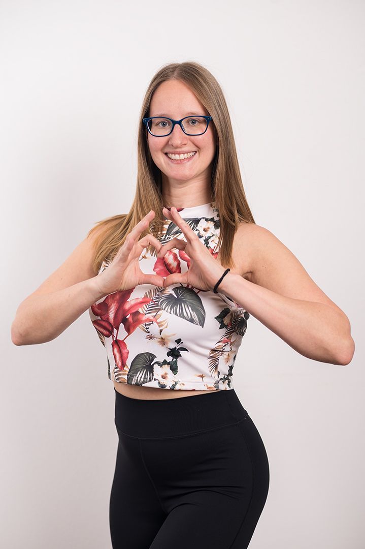 A woman wearing glasses and a floral crop top is making a heart shape with her hands.