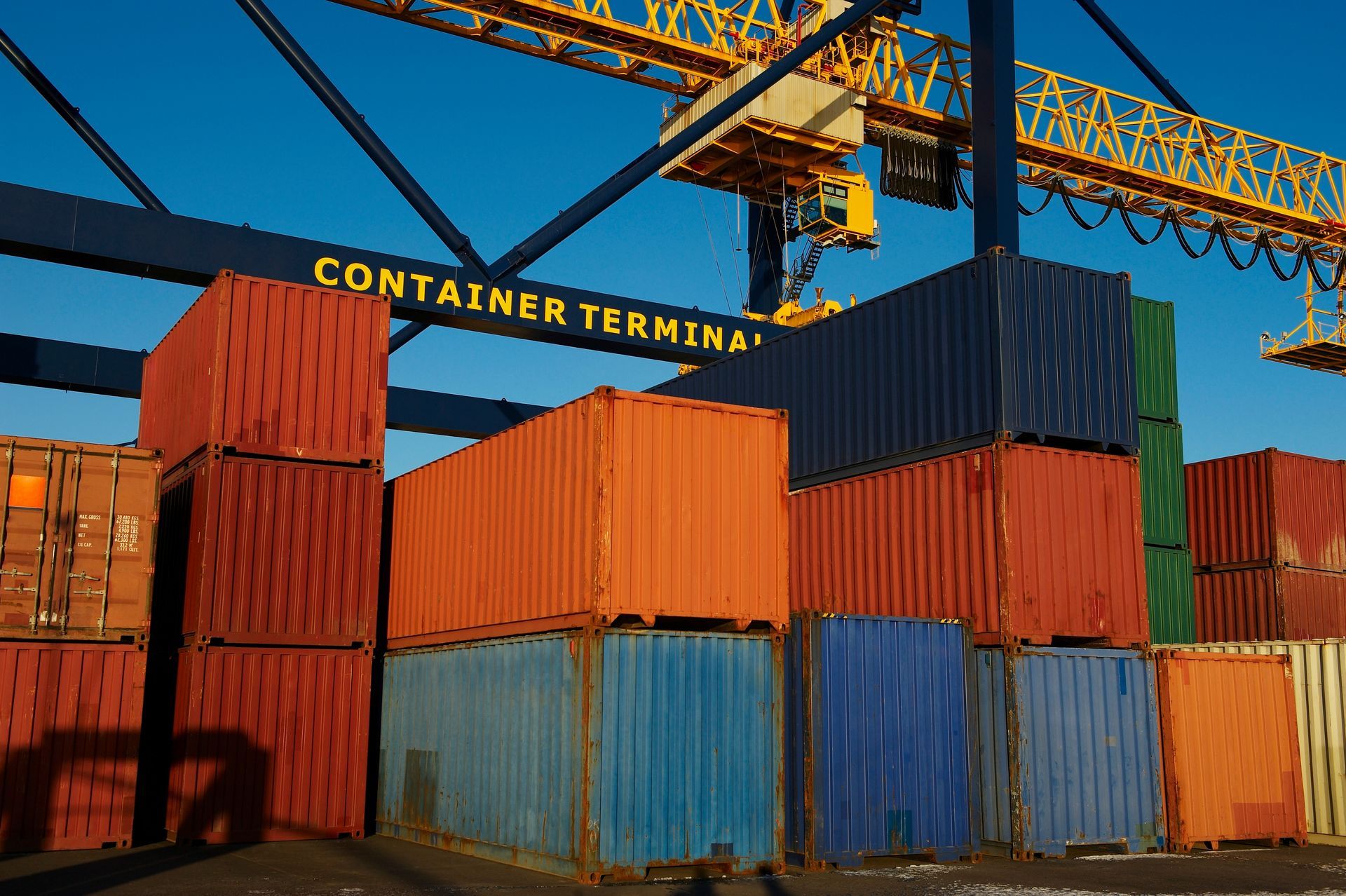 Colorful shipping containers stacked at a container terminal with cranes overhead.