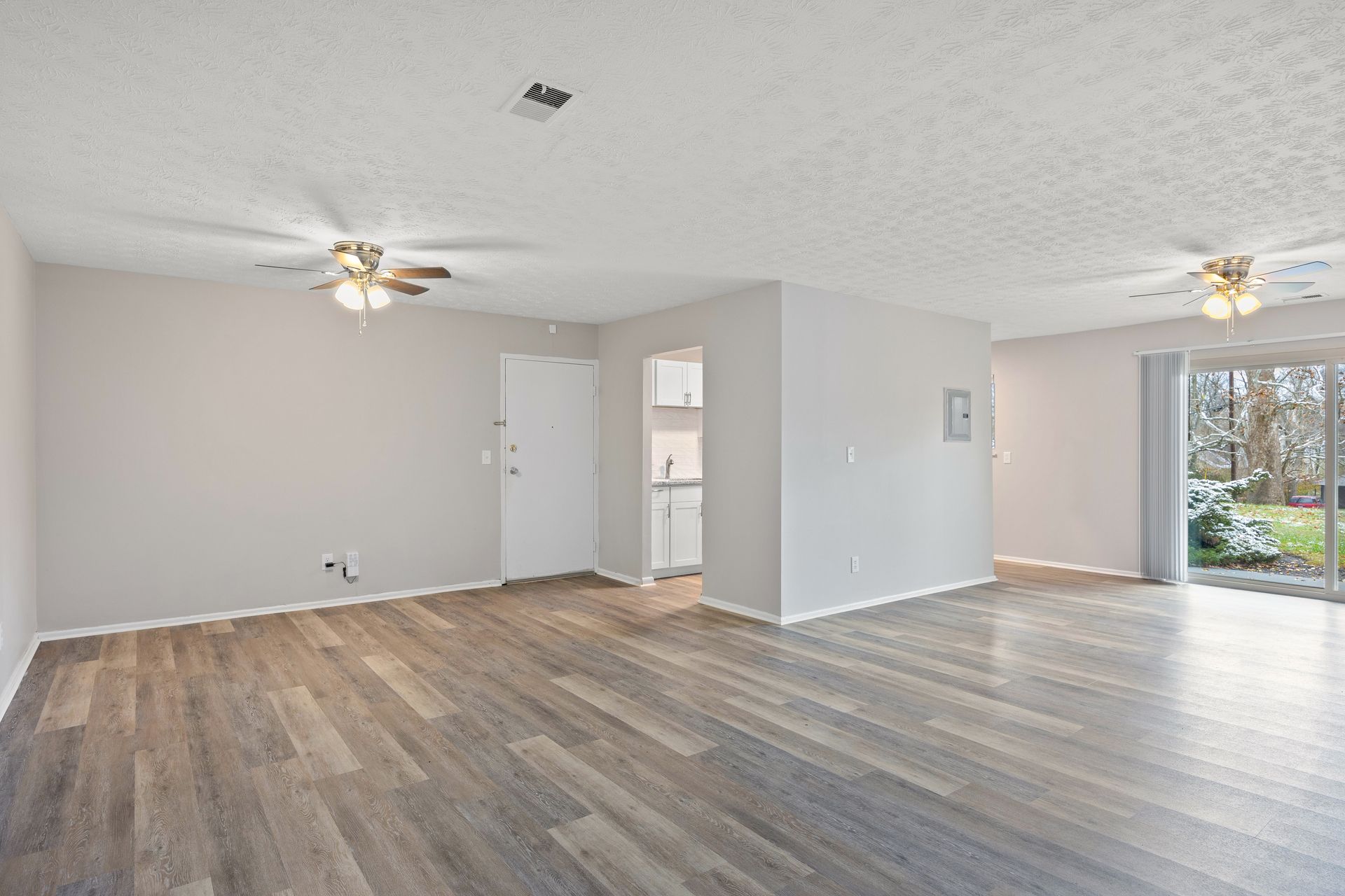 Open-concept living room with ceiling fan, large windows, and wood-style flooring.