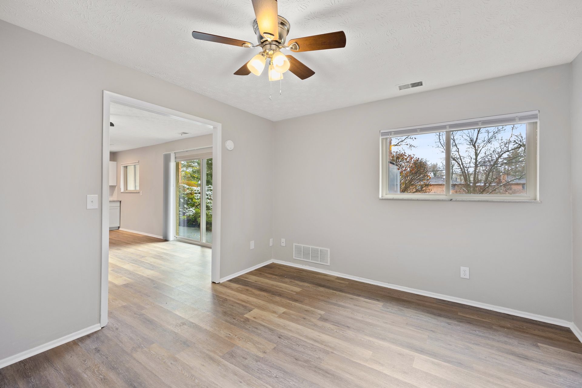 Apartment bedroom with large window, ceiling fan, and wood-style flooring.