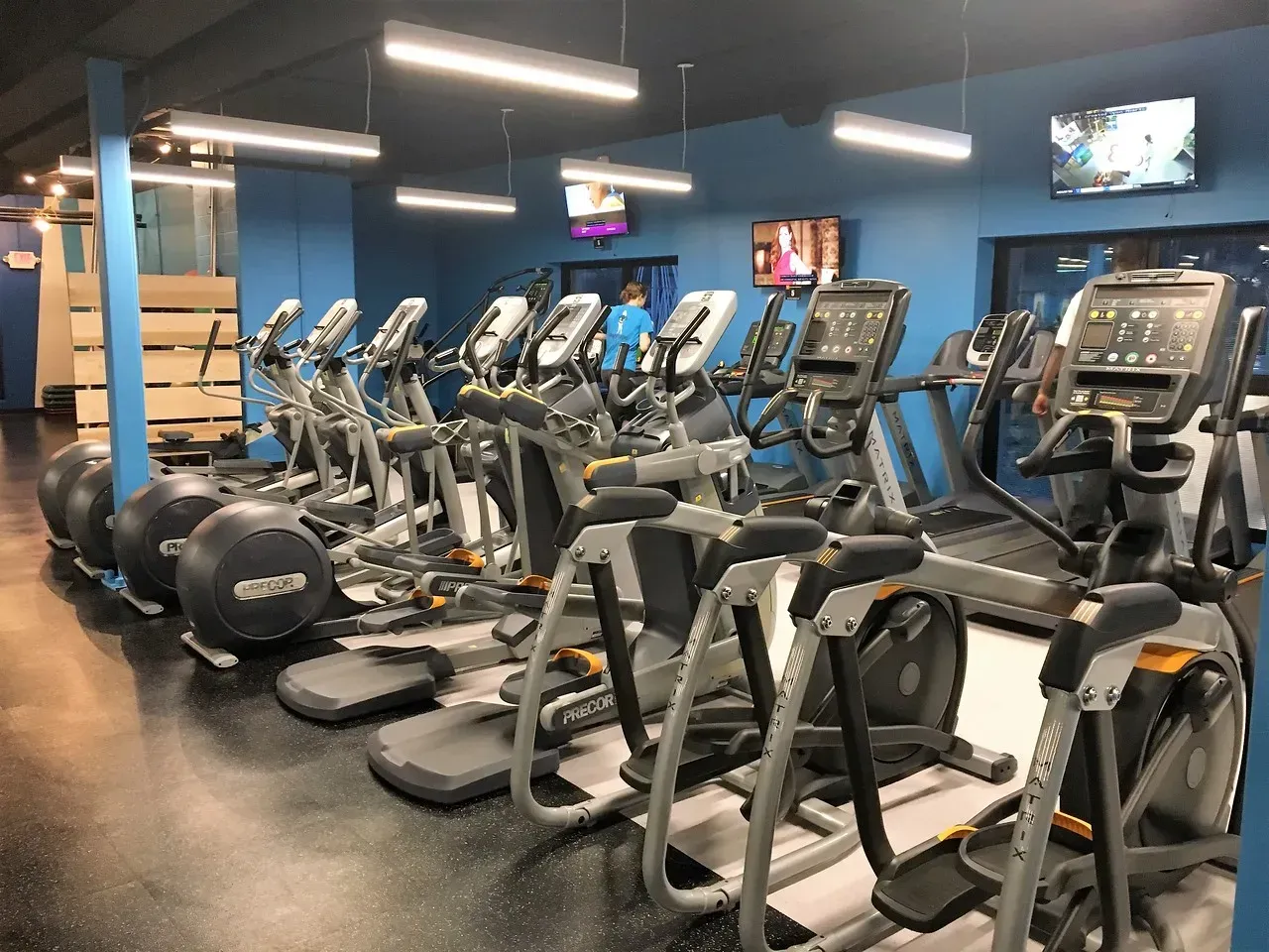 Apartment fitness center with treadmills, ellipticals, and mounted TVs.