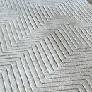 A textured, light-colored area rug featuring a repeating geometric pattern of carved, parallel zig-zag lines.
