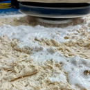 A floor scrubber machine cleans a beige carpet covered in white foam.