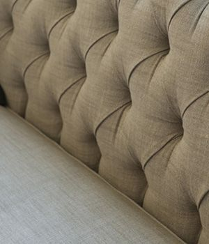 Close-up of a tan, tufted fabric sofa back with visible diamond-pattern stitching and folds in the upholstery.