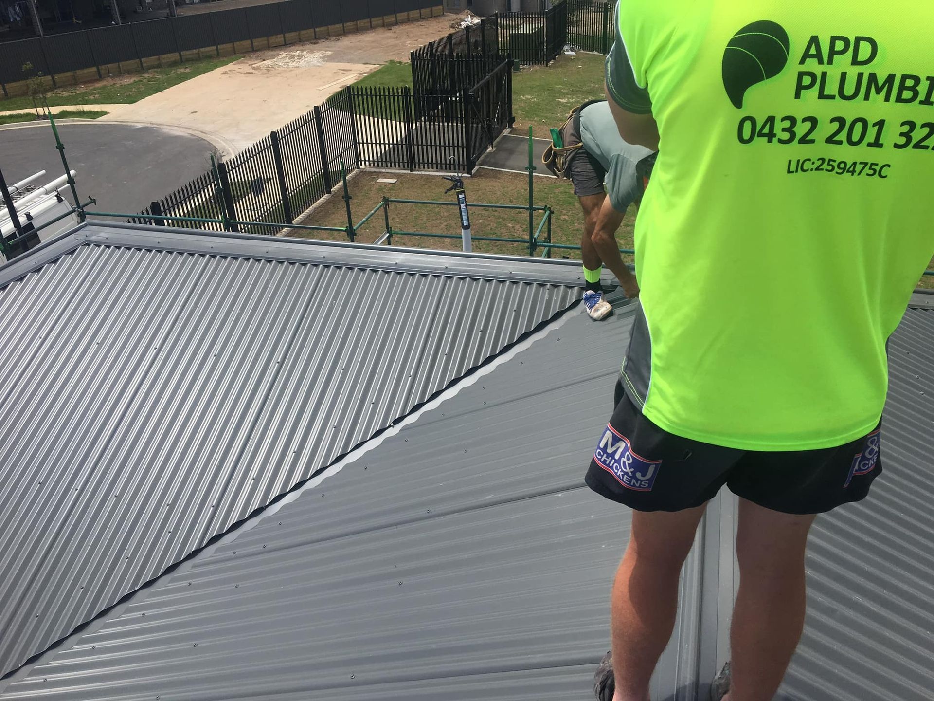 A Person in a Bright Neon Shirt Stands on a Metal Roof — APD Plumbing In Beechwood, NSW