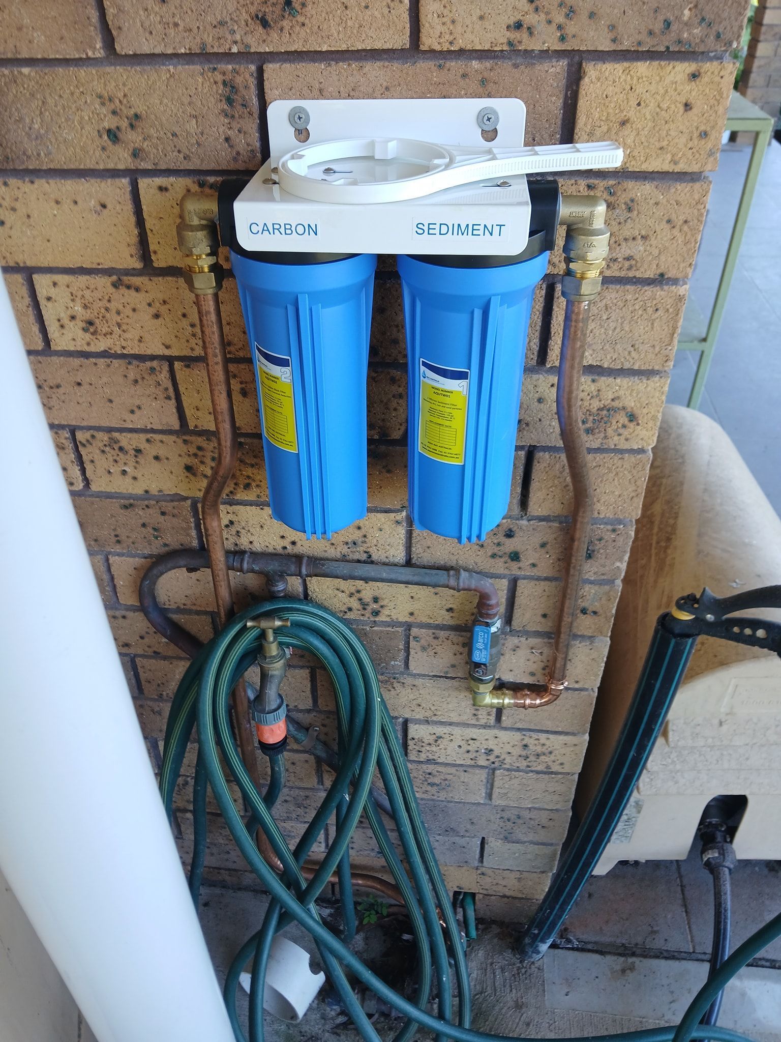 Two Blue Water Filter Housings Mounted on a Brick Wall — APD Plumbing In Beechwood, NSW
