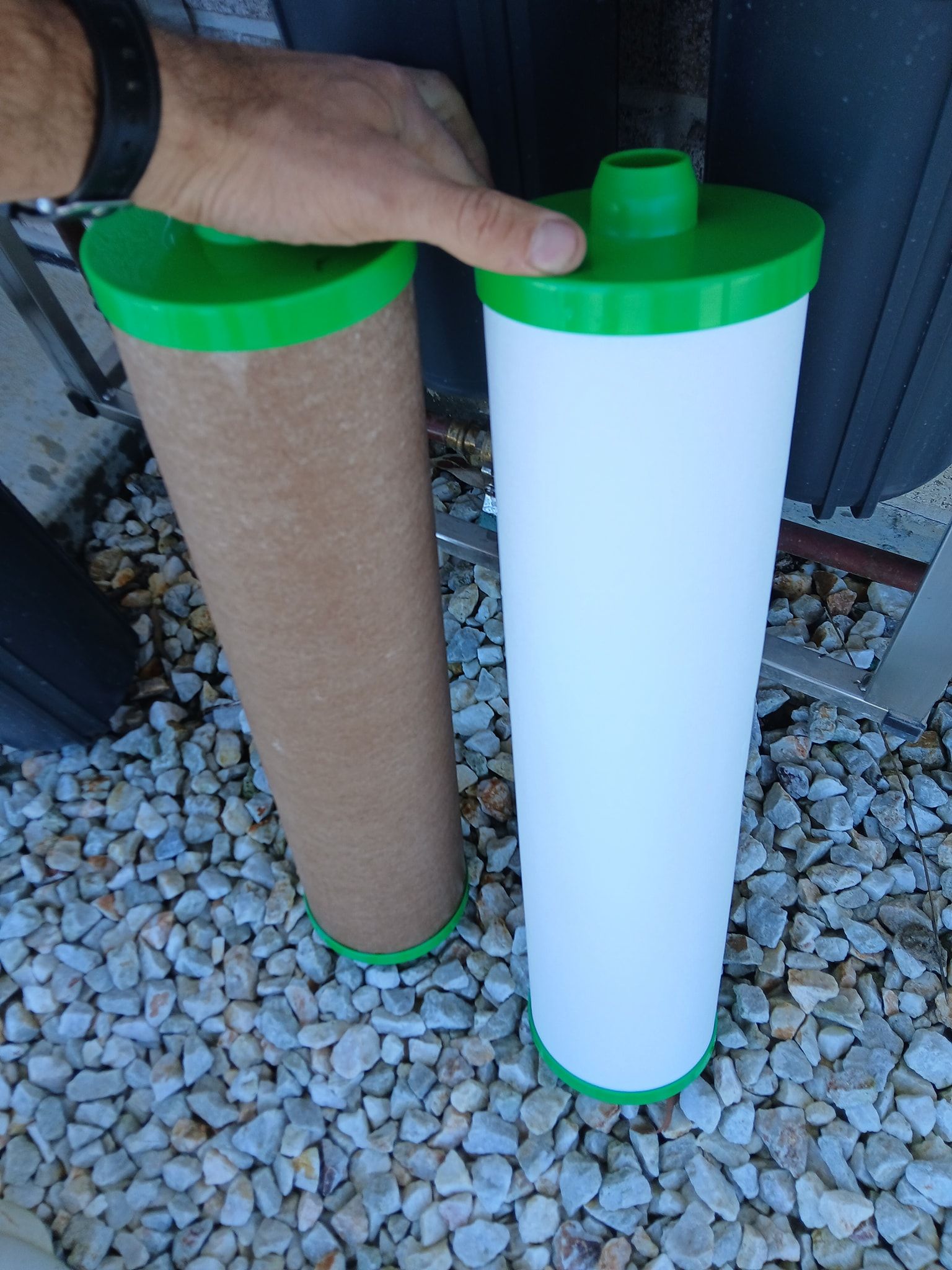 A Hand Holds a Used Brown Water Filter Next to a New White Water Filter — APD Plumbing In Beechwood, NSW