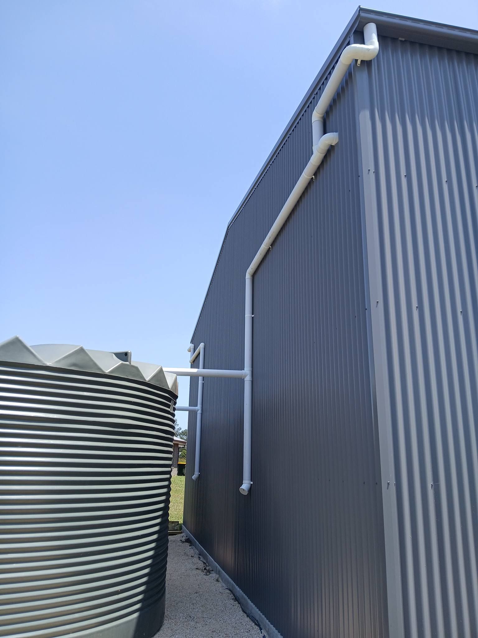 Corrugated metal shed beside a large ribbed water tank under a clear blue sky