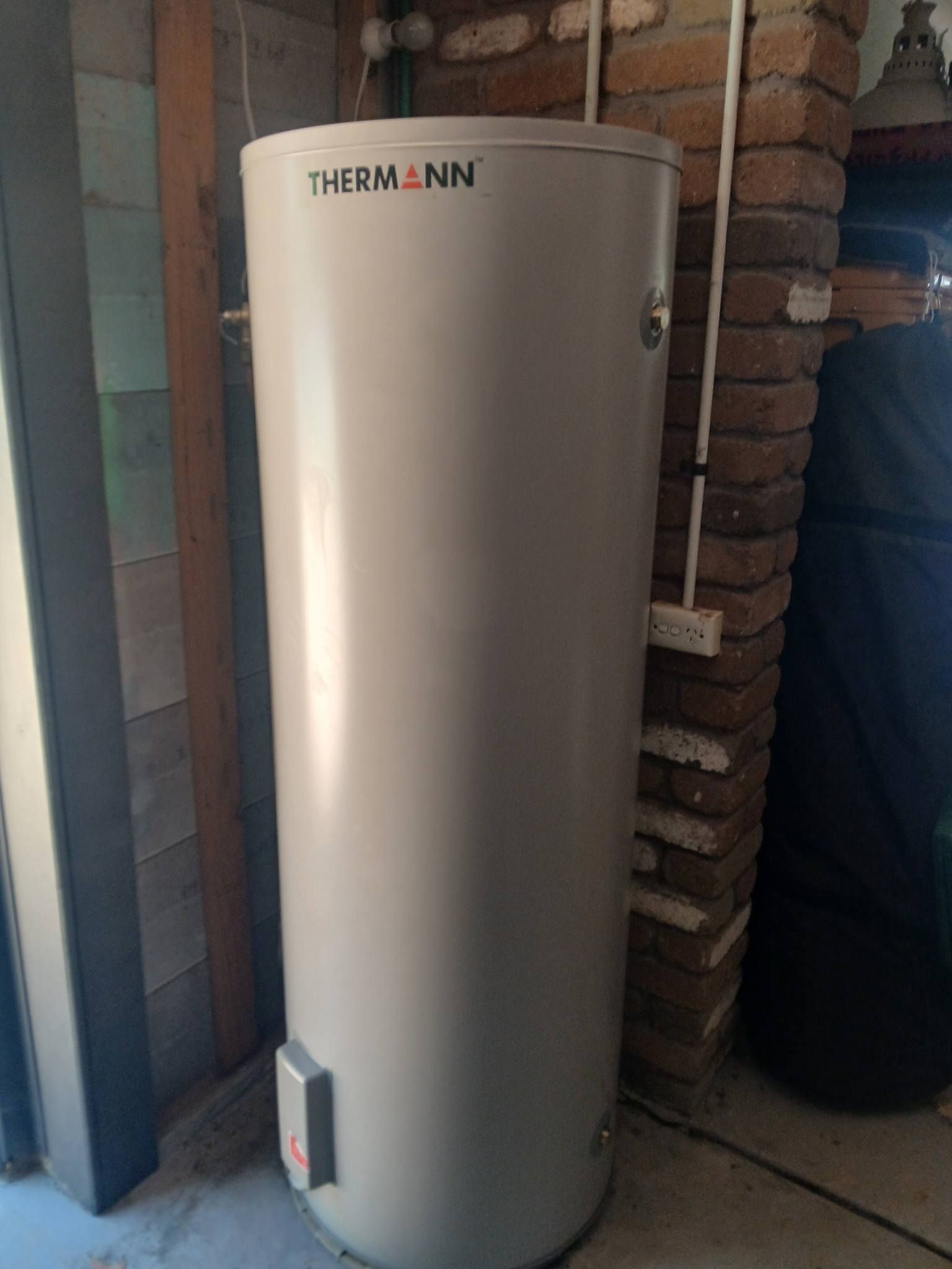 Tall gray water heater tank in a utility area beside exposed brick walls.