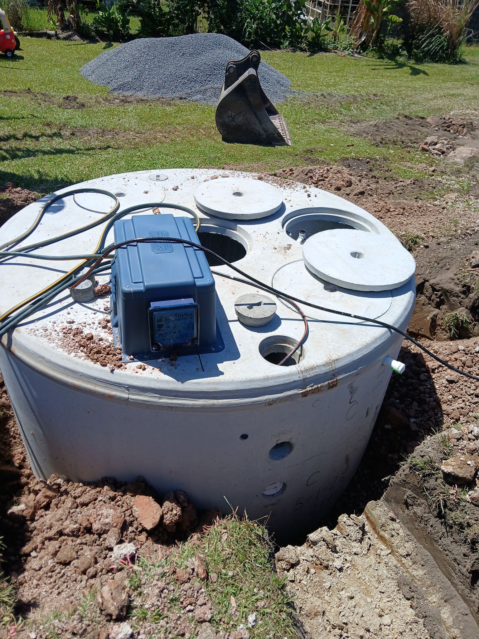 Round concrete utility cover with coiled hose and a small pump/gauge assembly on grass - APD Plumbing In Beechwood, NSW