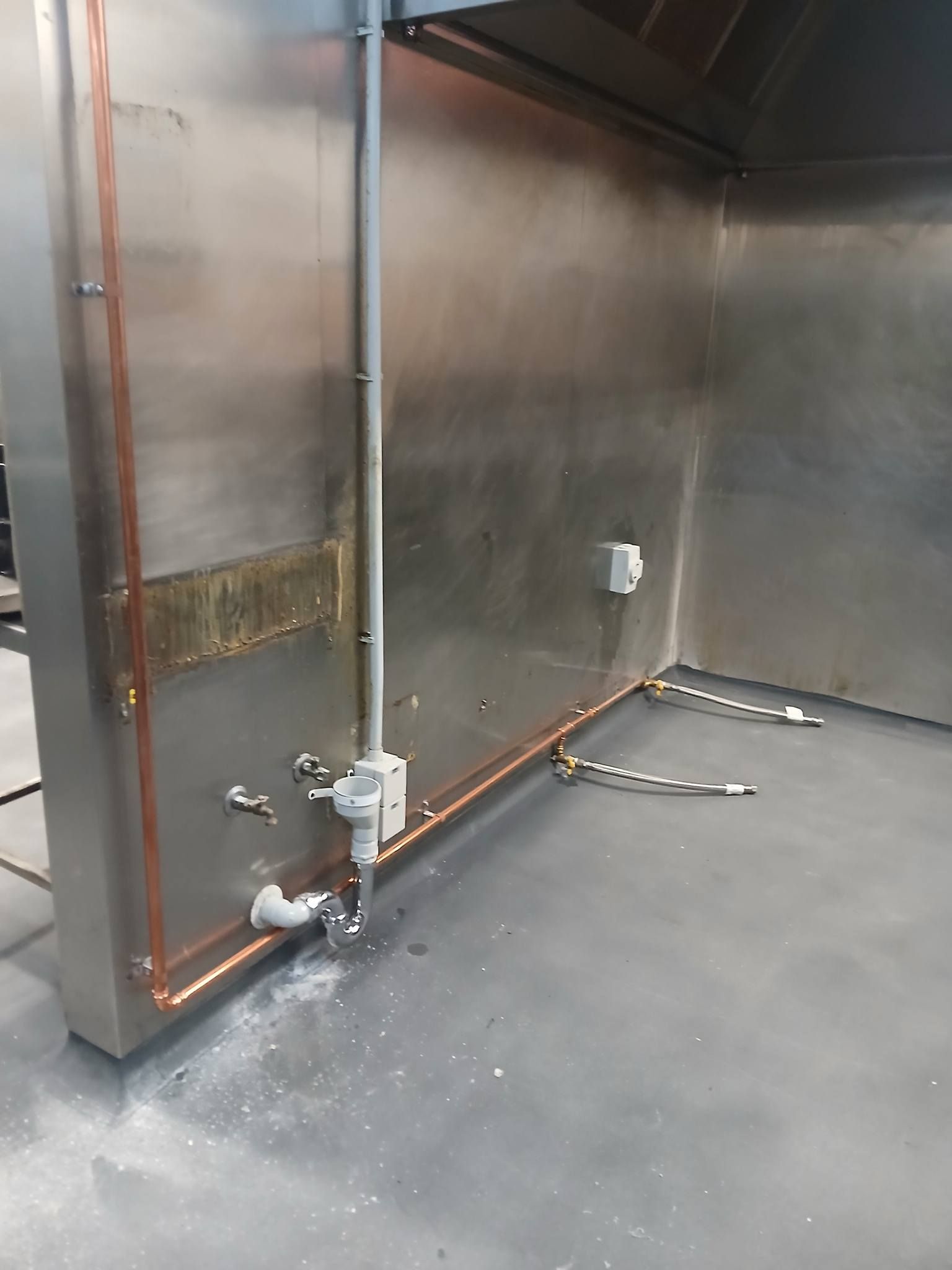 Industrial stainless steel equipment with exposed pipes and valves on a gray floor.