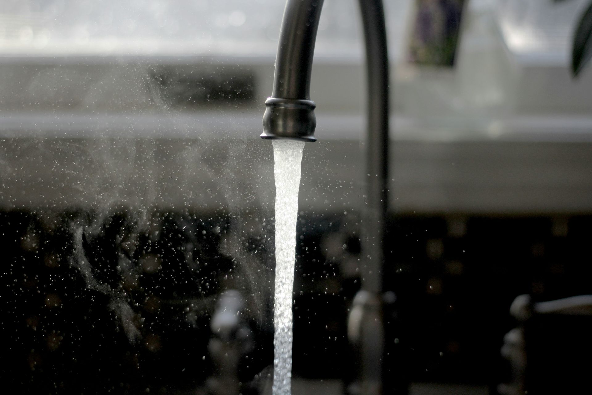 Running kitchen faucet with water streaming into a sink, splashing in a dark background