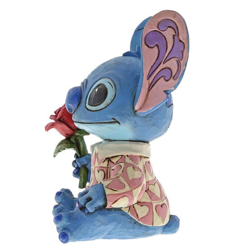 Een Stitch-figuurtje met een rode roos in zijn hand, gekleed in een roze jas met hartjespatroon.