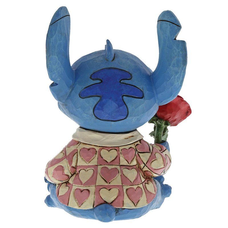 Een Stitch-figuurtje, blauw met grote oren, dat een rode roos vasthoudt en een roze jasje met hartjespatroon draagt.