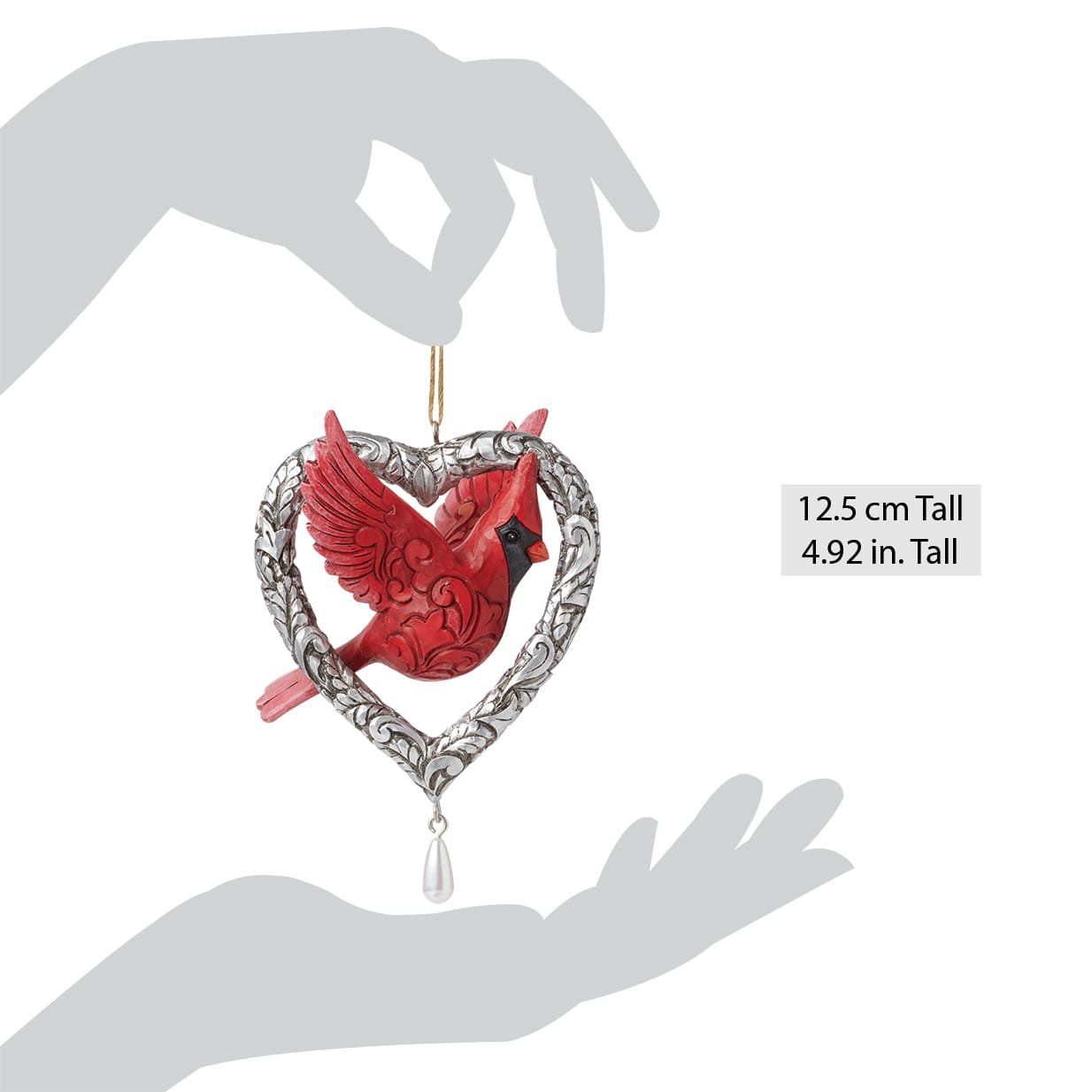 Een rode kardinaal in een hartvormig ornament. Het ornament wordt in een hand gehouden.