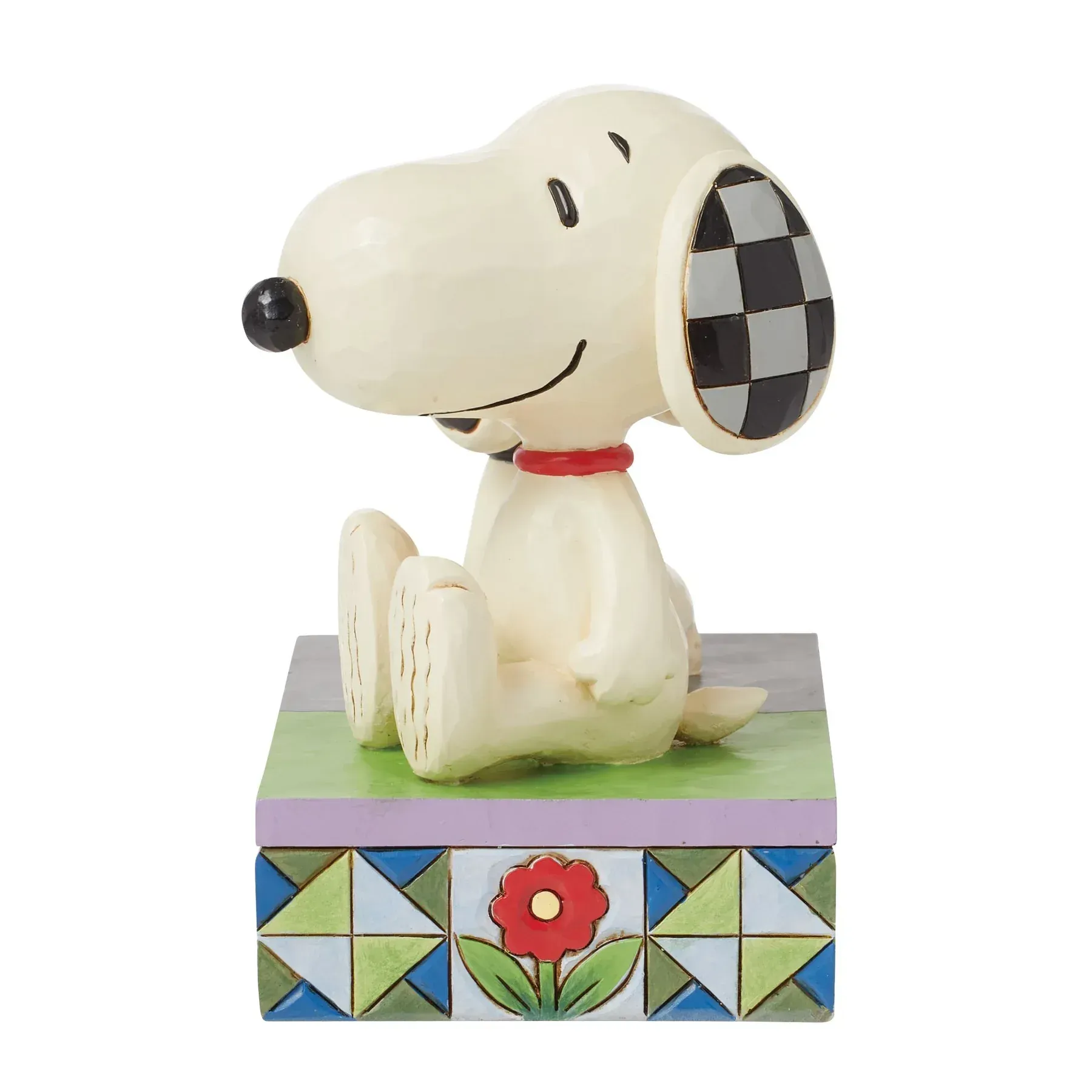Een Snoopy-figuurtje dat op een blok zit, met geblokte oren en een rode halsband.