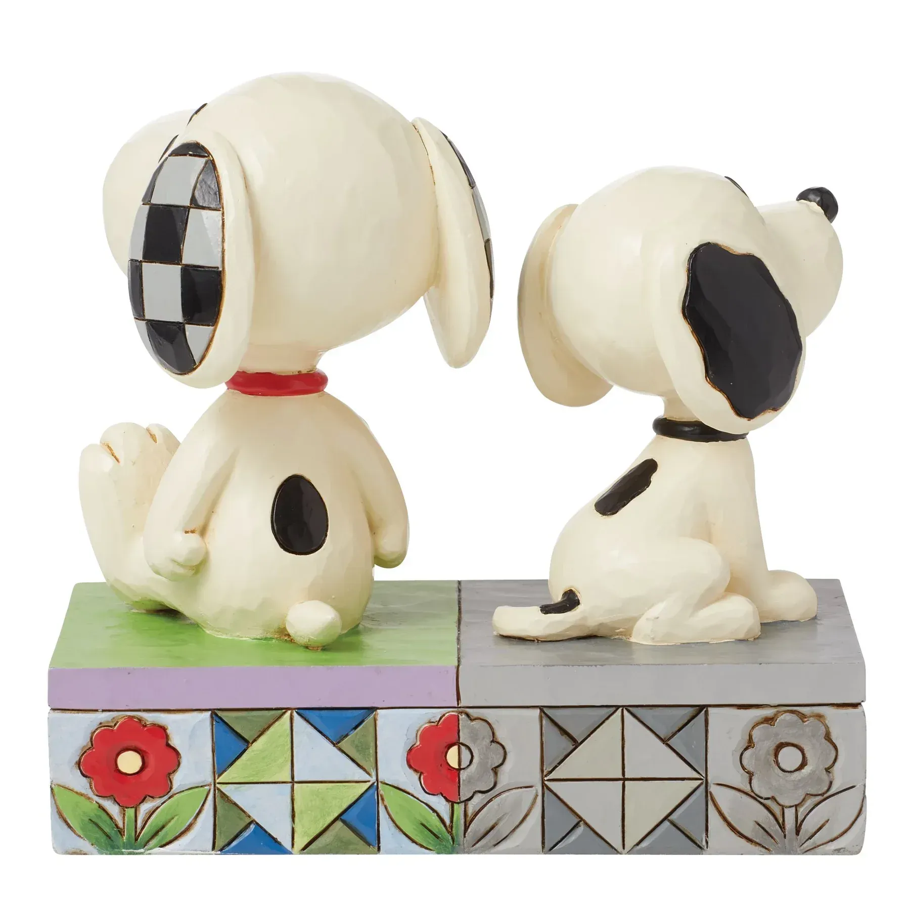 Twee Snoopy-beeldjes, waarvan één met geblokte oren, staan op een versierde sokkel.