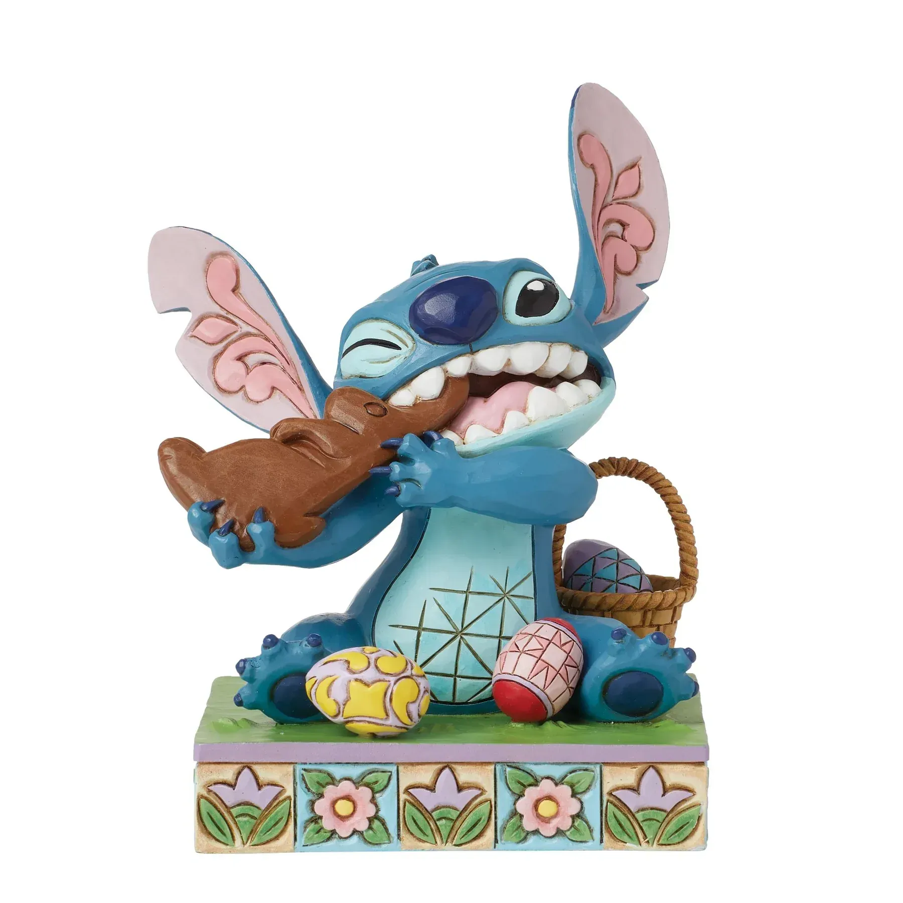 Een Stitch-figuurtje dat een chocoladekonijntje eet; paaseieren en een mandje liggen er vlakbij. Blauwe, bruine en pastelkleuren.