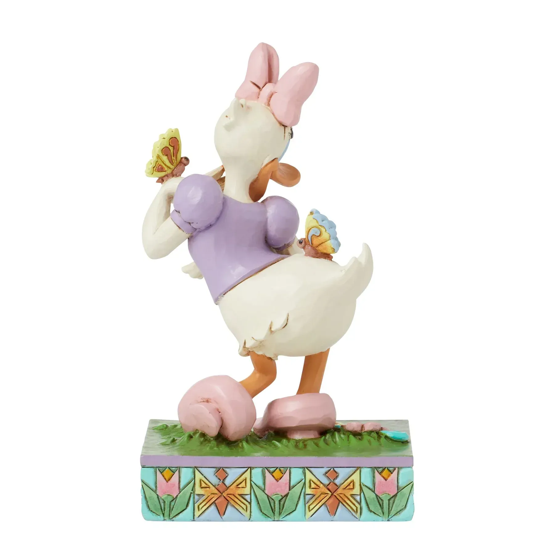 Een beeldje van Daisy Duck met vlinders, met een roze strik in haar haar, lachend, staand op een versierde sokkel.