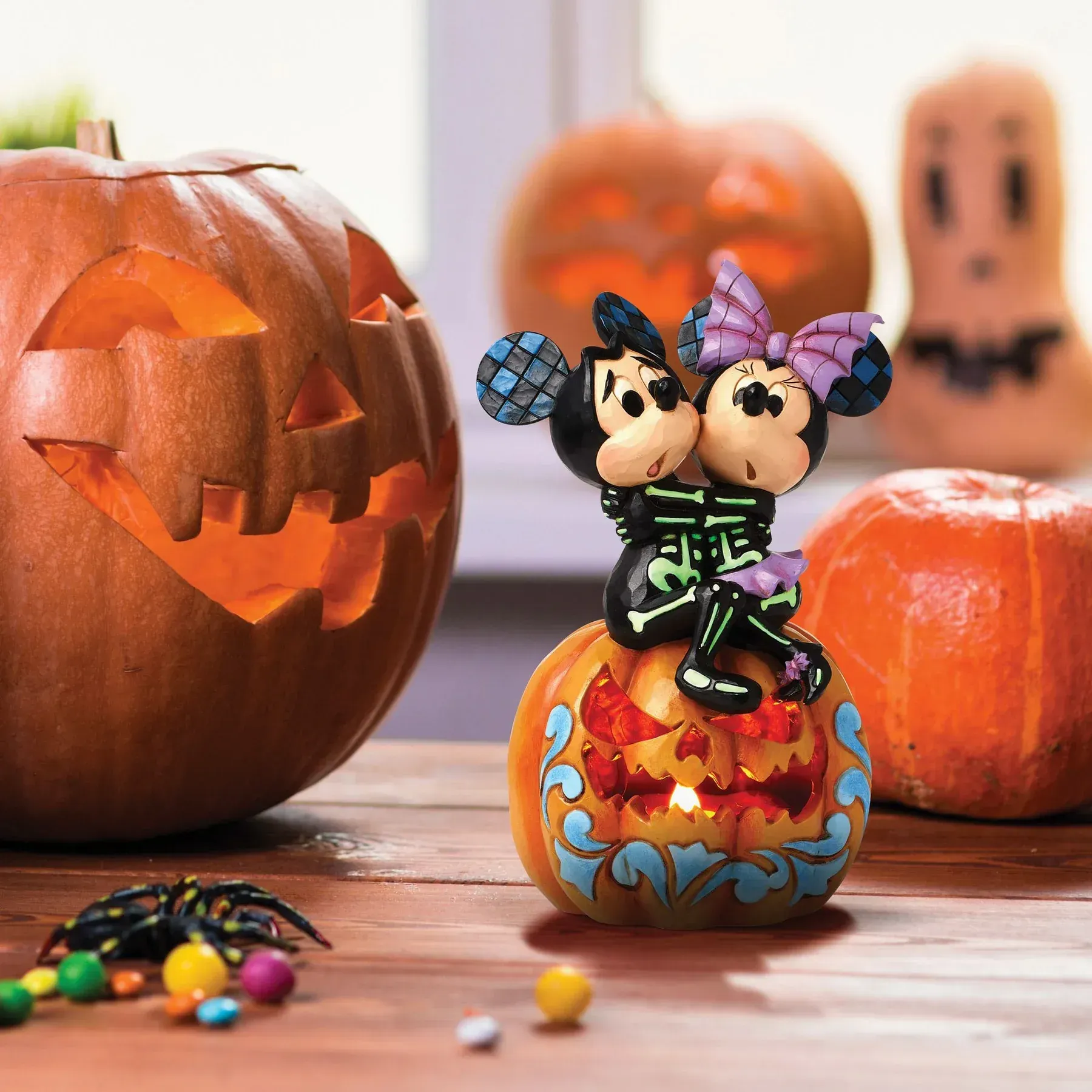 Mickey en Minnie Mouse Halloween-figuurtjes op een uitgeholde pompoen, met jack-o'-lantern en snoepversieringen.