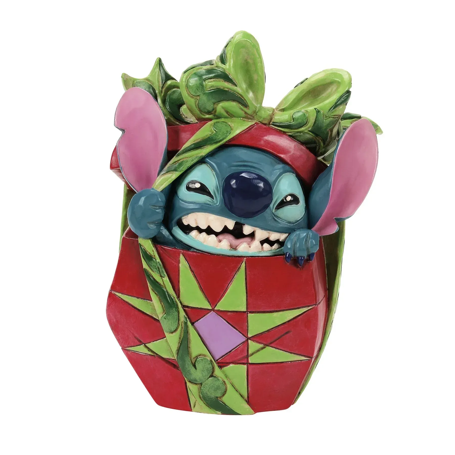 Een Stitch-figuurtje in een rode geschenkdoos met groene en roze versieringen. Stitch grijnst en gluurt naar buiten.