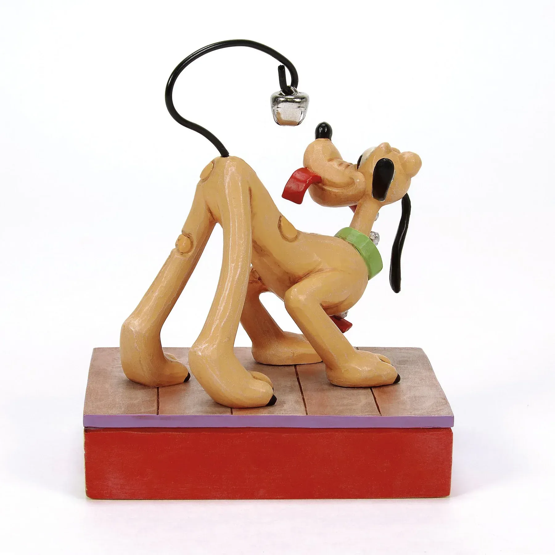 Een Pluto-figuurtje, omhoogkijkend met uitgestoken tong, staat op een houten platform. Boven zijn hoofd hangt een zwart draadje met een klein zilveren voorwerp.