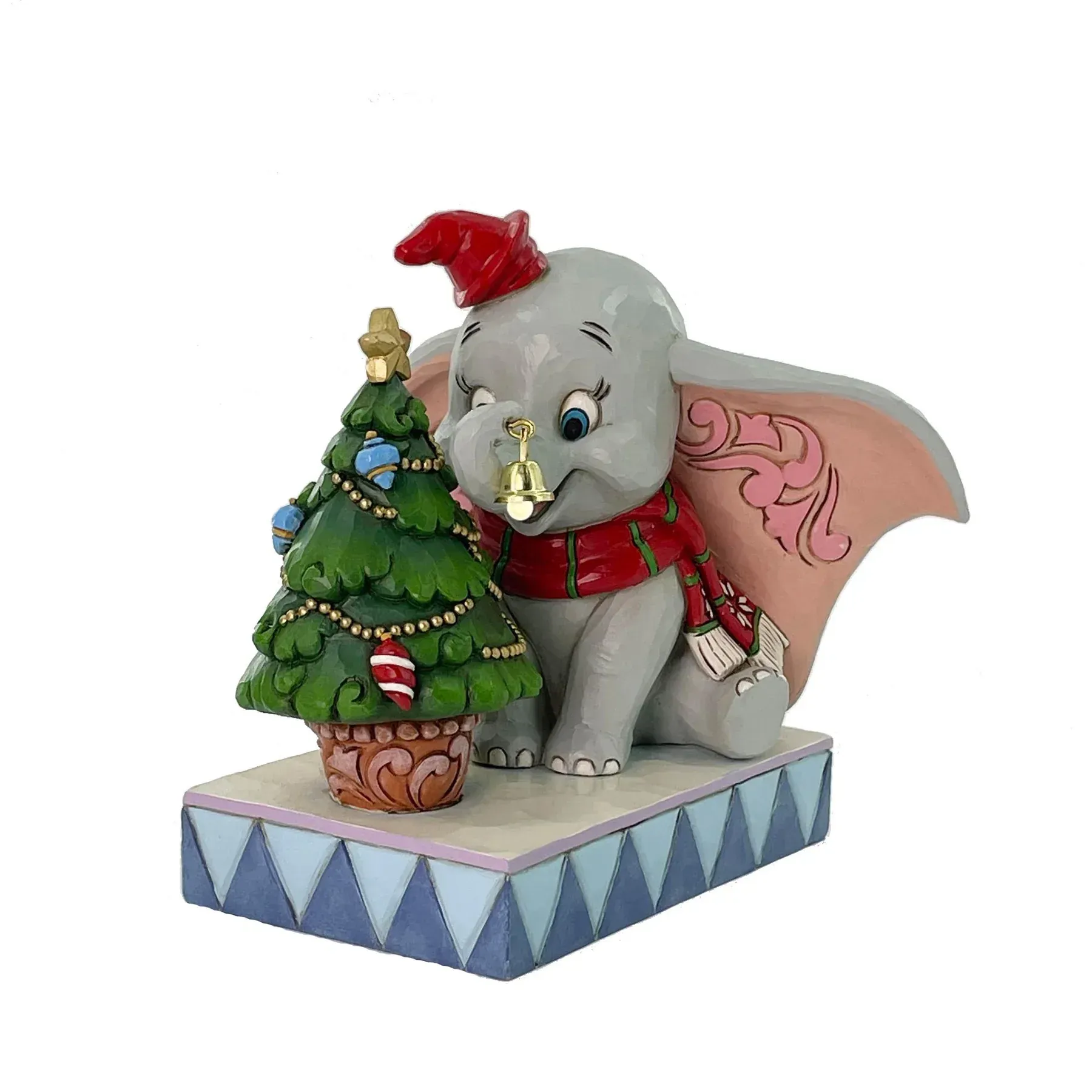 Een Dumbo-figuurtje met een kerstmuts op, naast een kerstboom, op een blauw-wit gestreepte sokkel.