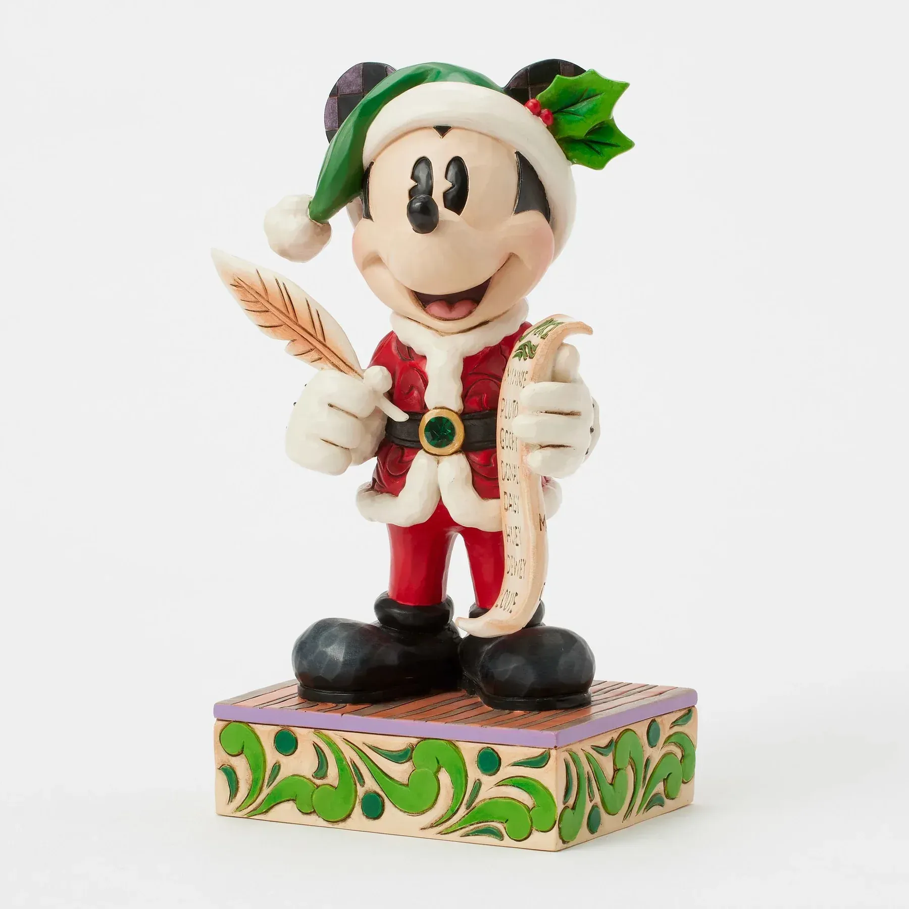Mickey Mouse, verkleed als Kerstman, met een veer en een perkamentrol met een kerstlijst, staat op een versierde sokkel.