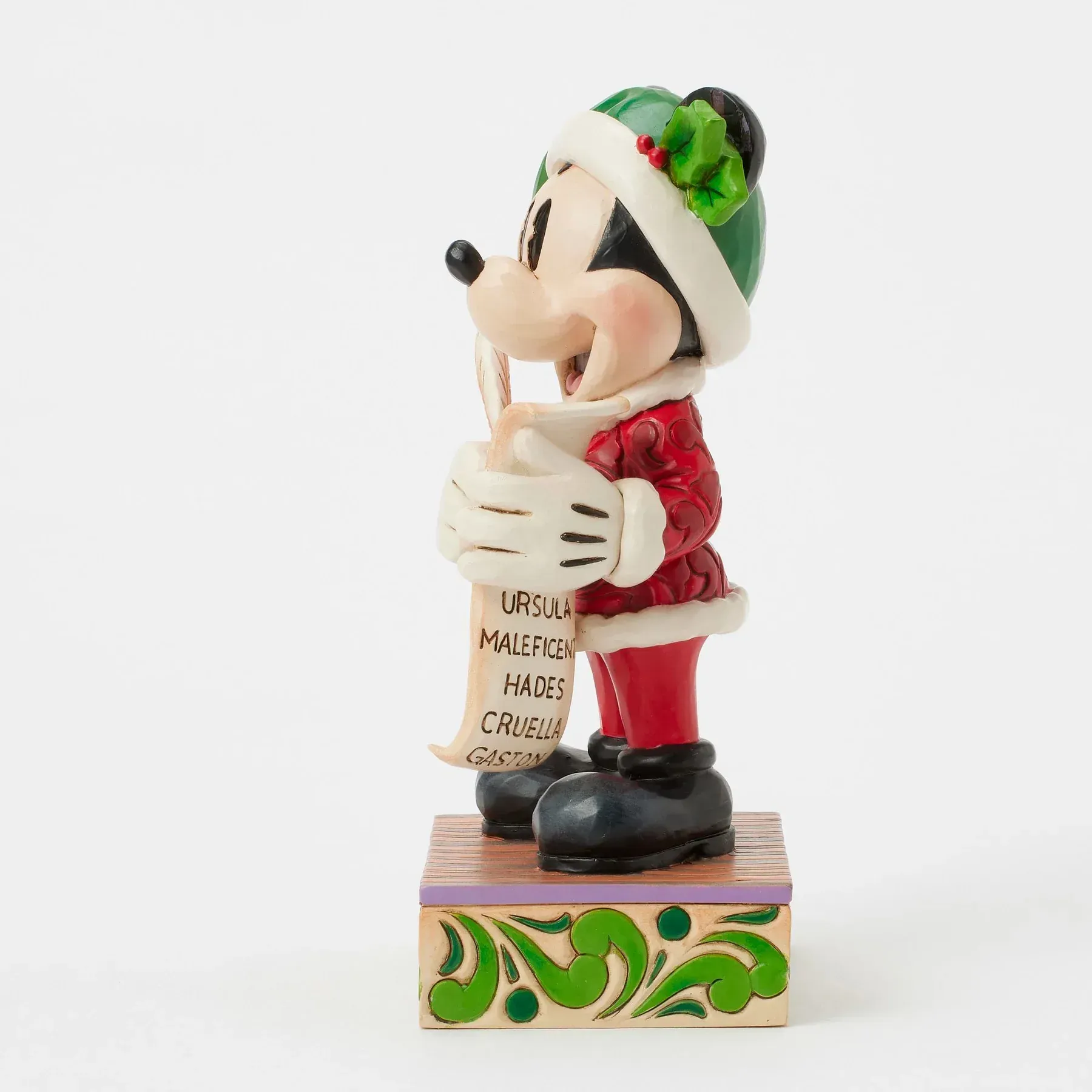 Een Minnie Mouse-figuurtje in een kerstmanpakje met een kerstlijstje in haar hand, staand op een versierde sokkel.