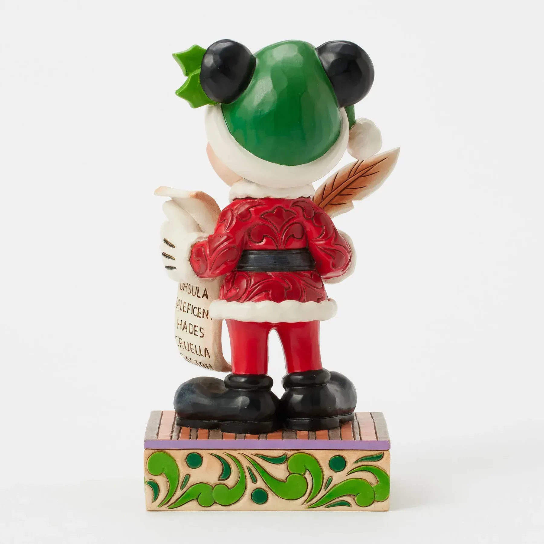 Achteraanzicht van een Mickey Mouse-figuurtje in een kerstmanpak, met een lijstje en een ganzenveer in zijn handen.