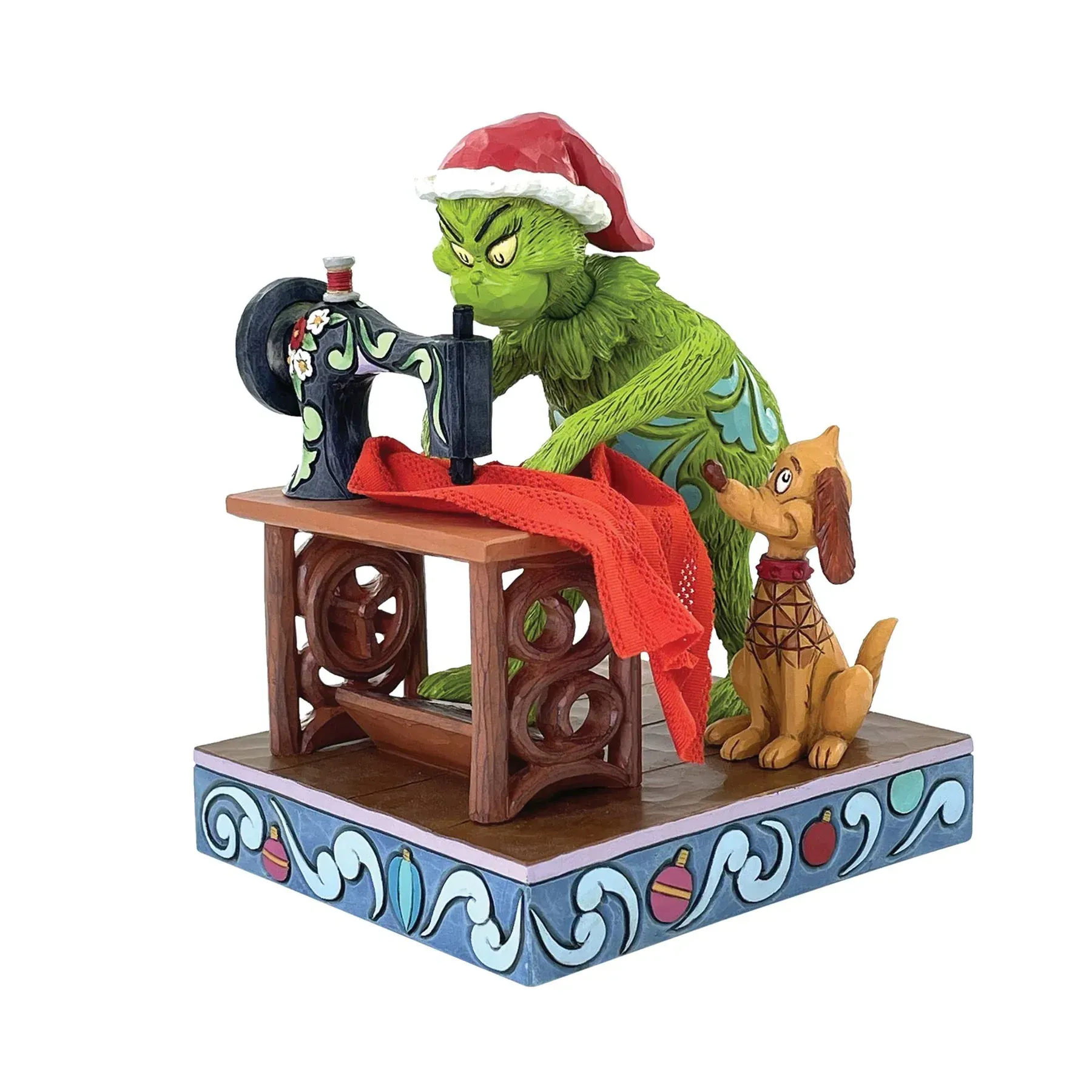De Grinch met een kerstmuts naait rode stof op een naaimachine, met Max de hond, op een versierde ondergrond.