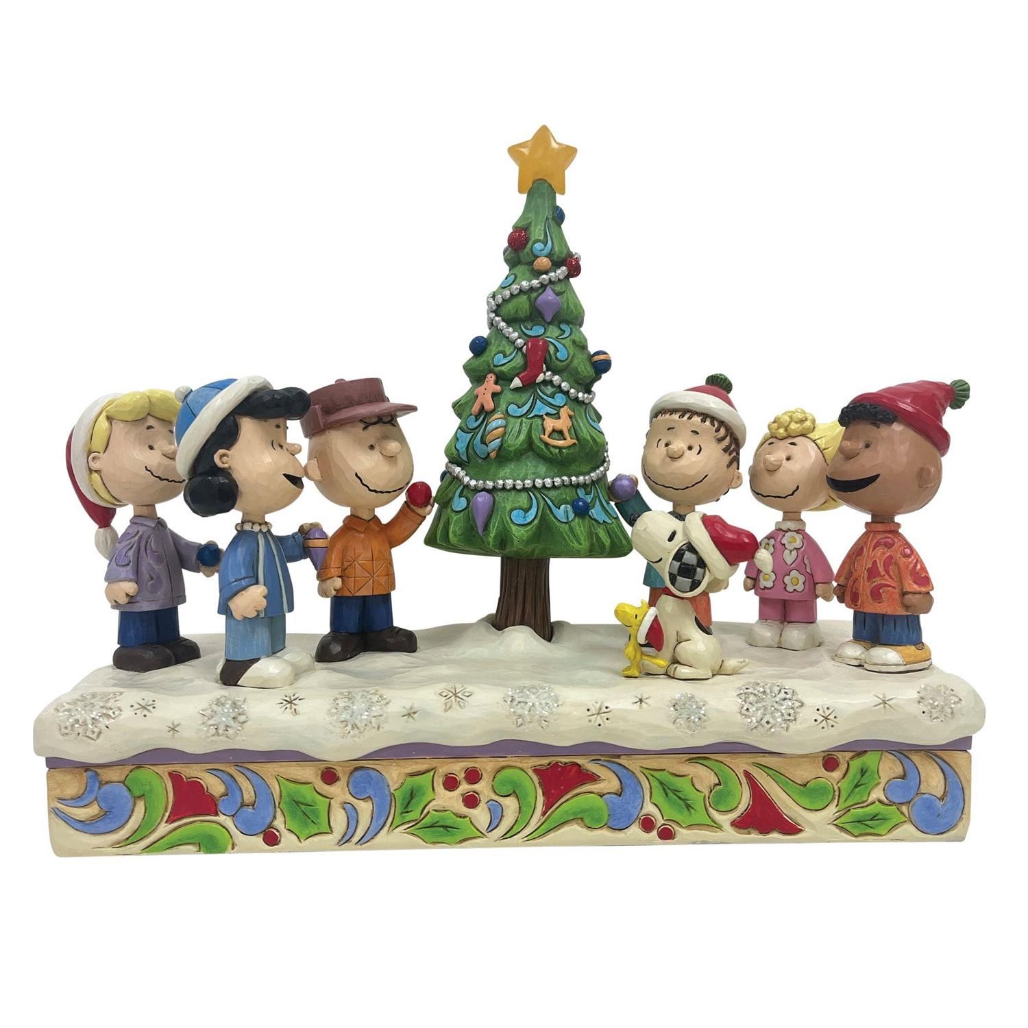 Peanuts-figuren rond een versierde kerstboom; beeldjes op een besneeuwde sokkel.