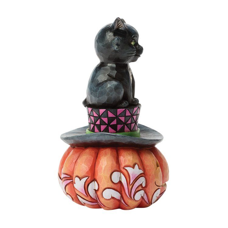 Een beeldje van een zwarte kat bovenop een hoed en een pompoen, met een Halloween-thema.