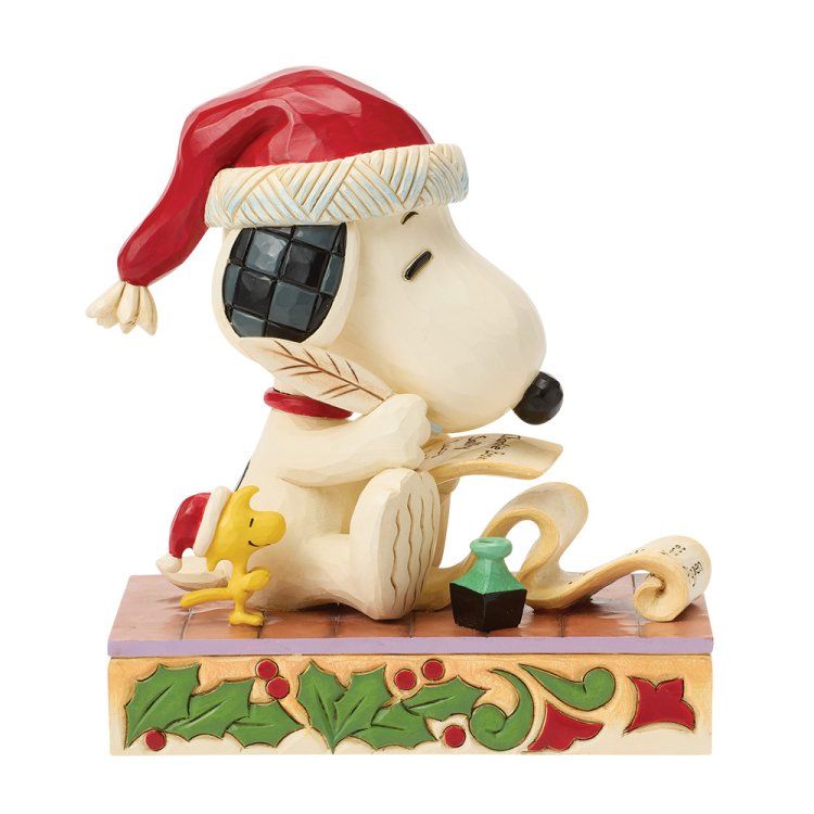 Snoopy met een kerstmuts op schrijft een lijstje, met Woodstock op een sokkel versierd met hulst.