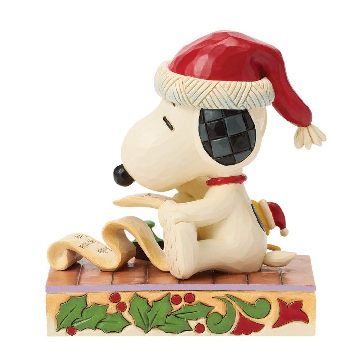 Snoopy met een kerstmuts op leest een lange kerstlijst, zittend op een versierde sokkel.