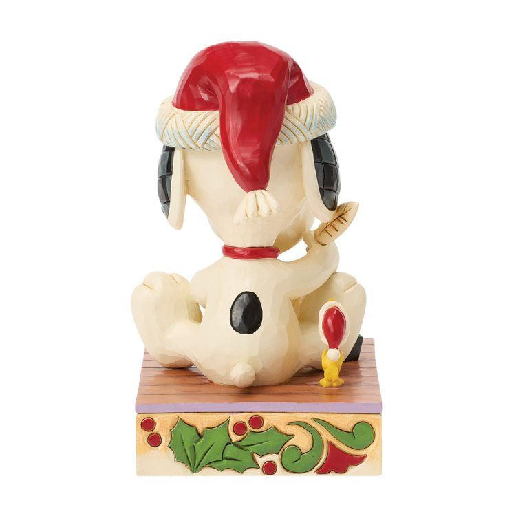 Snoopy met een kerstmuts op, zittend op een versierde doos, met een kaars in zijn hand.