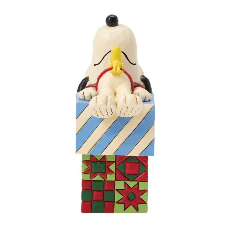 Een Snoopy-figuurtje zit op een kleurrijke geschenkdoos, met gesloten ogen en een rode sjaal.