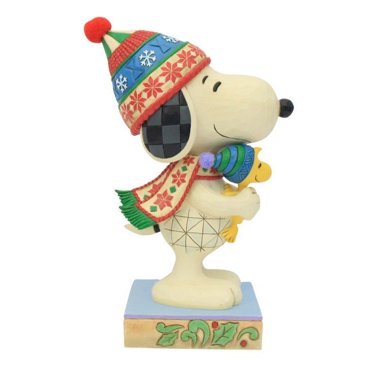 Een Snoopy-figuurtje met wintermuts en sjaal, die Woodstock vasthoudt, op een decoratieve sokkel.