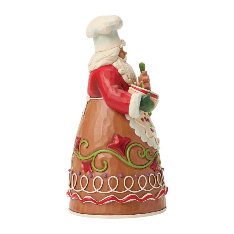 Een kerstmanfiguurtje met koksmuts en schort, die een kom en een wortel vasthoudt.