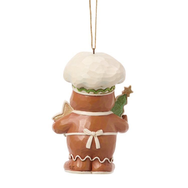 Een peperkoekkokje als ornament, met een witte koksmuts en schort, die een ster en een boom vasthoudt.
