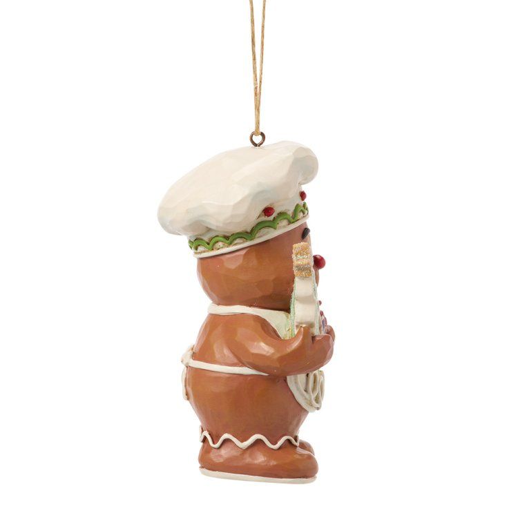 Een peperkoekkokfiguurtje houdt een boom en een sterkoekje vast, en draagt ​​een hoed en een schort.