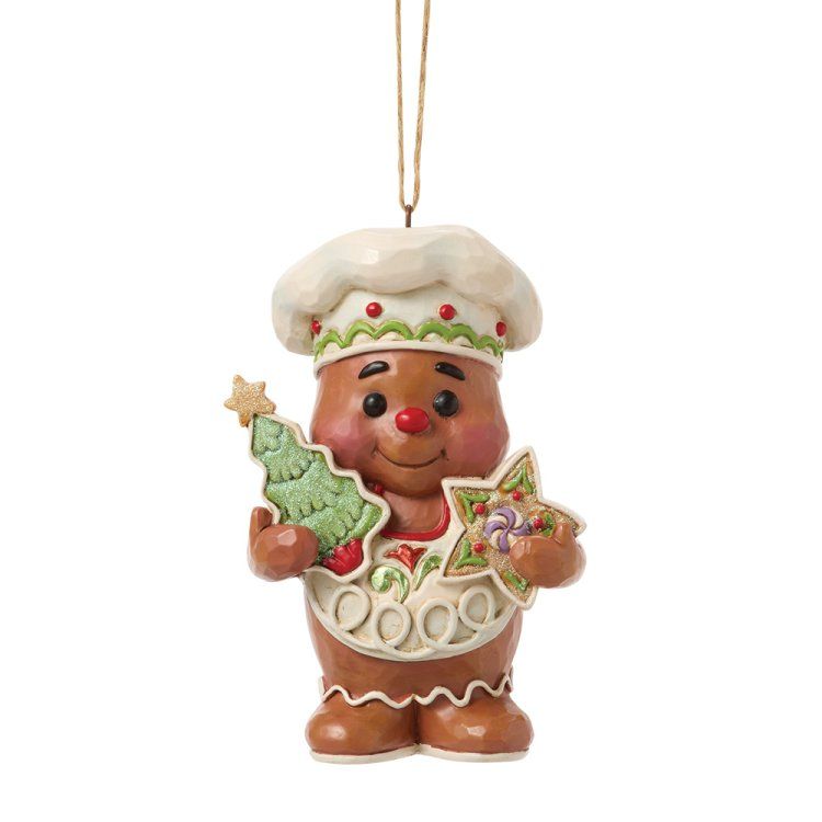 Een peperkoekkokfiguurtje houdt een boom en een sterkoekje vast, en draagt ​​een hoed en een schort.