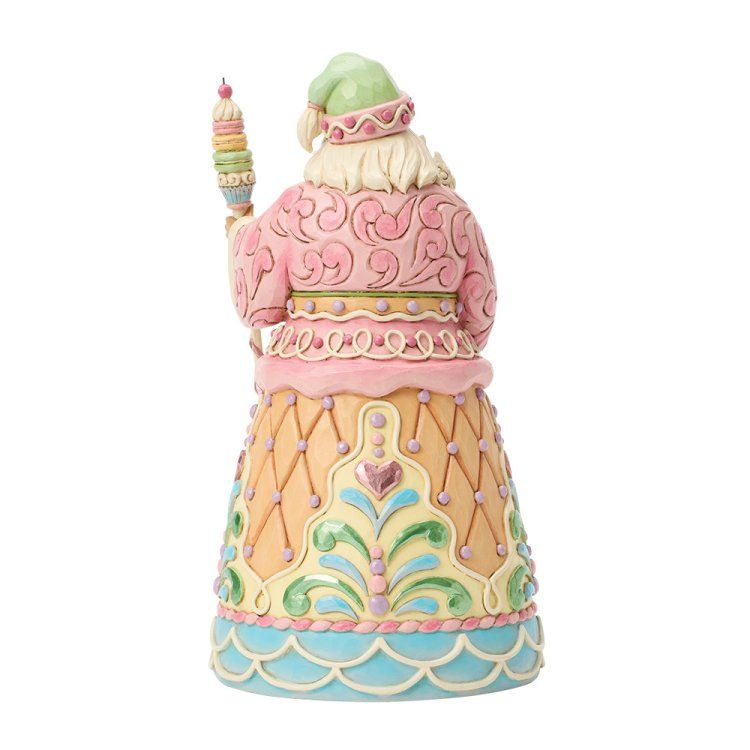 Een pastelkleurig kerstmanfiguurtje met een kaars en een staf met een gekrulde bovenkant, gekleed in een roze gewaad en een groene muts.