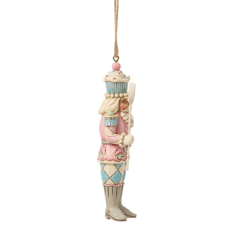 Een pastelroze notenkrakerornament met een beige touwtje, waarin een stafje staat.