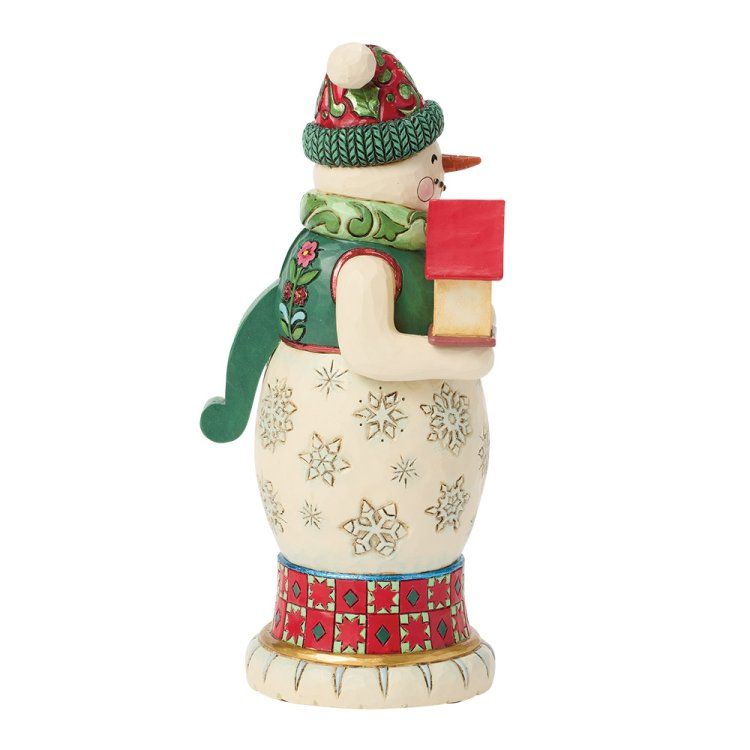 Een sneeuwpopfiguurtje dat een rood cadeautje vasthoudt, een muts en sjaal met een patroon draagt.